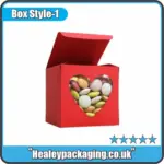 Red candy box with heart-shaped window displaying colourful coated sweets.