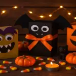 Fun Halloween-themed boxes decorated as monsters, bats, and pumpkins surrounded by candy corn, candles, and mini pumpkins on a festive wooden background.