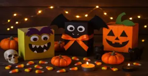 Fun Halloween-themed boxes decorated as monsters, bats, and pumpkins surrounded by candy corn, candles, and mini pumpkins on a festive wooden background.