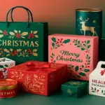 Festive Christmas packaging boxes and gift tins in red, green, and gold with holiday-themed designs including holly, snowflakes, ribbons, and decorative patterns.