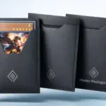 Black trading card sleeves by Healey Packaging holding collectible cards on grey background.